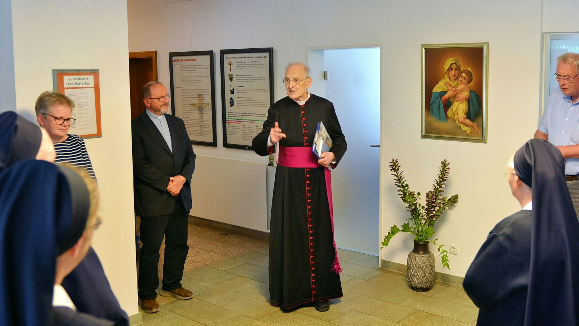 Prälat Helmut Moll gestikuliert mit dem rechten Arm. Im Raum mit ihm stehen Nonnen und drei weitere Personen.