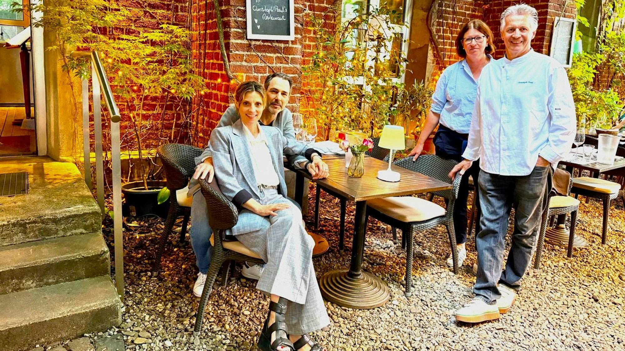 Ein Paar sitzt im Innenhof eines Restaurants, ein Paar steht neben seinem Tisch.