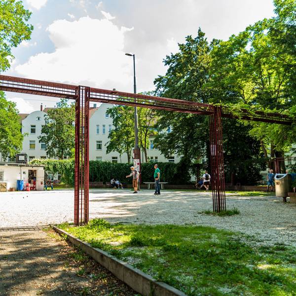 Ein Schotterplatz ist zu sehen, Leute spielen darauf Boule.