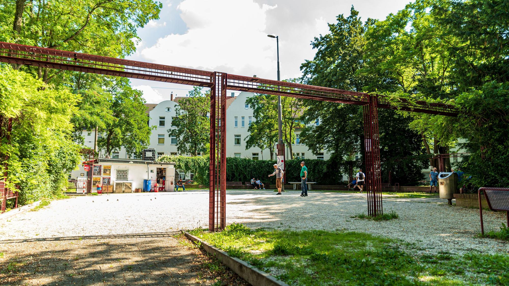Ein Schotterplatz ist zu sehen, Leute spielen darauf Boule.