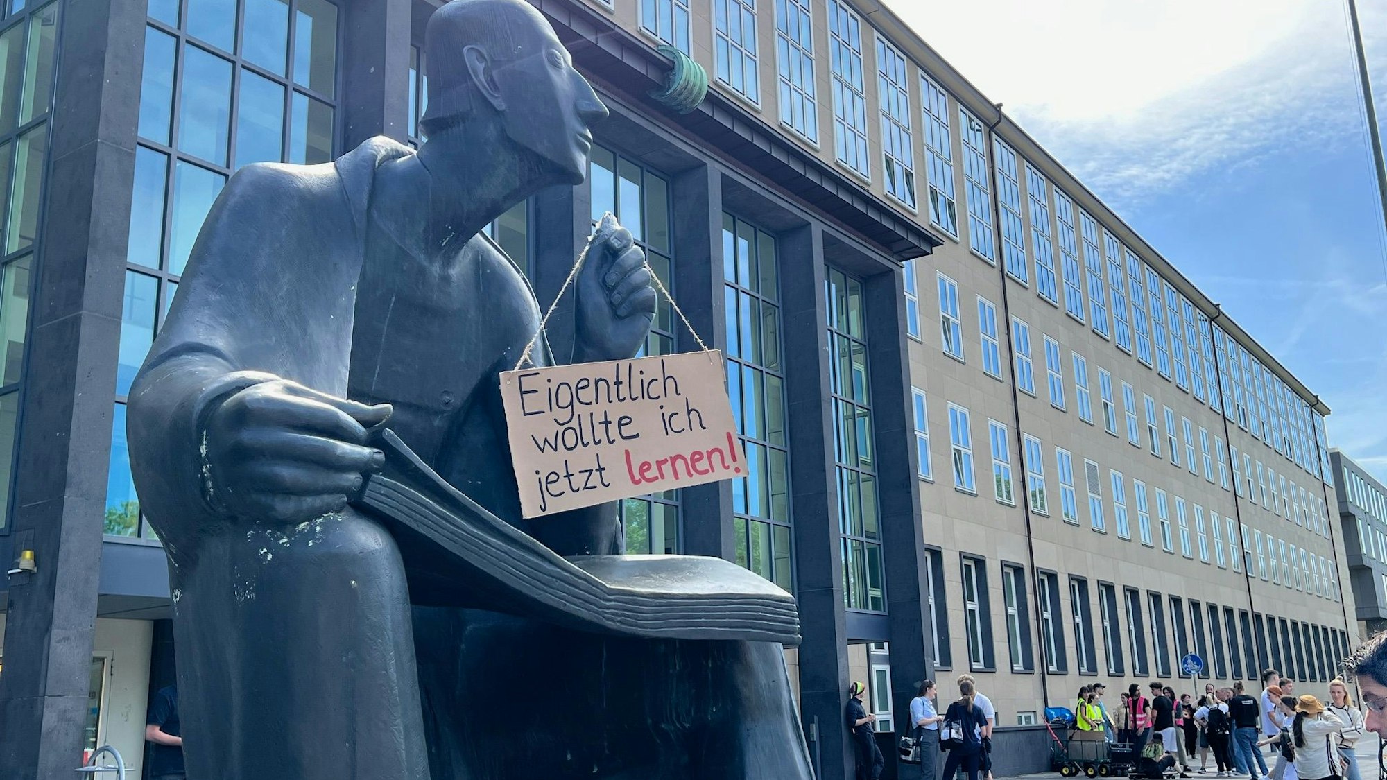 Albertus-Magnus-Statue vor dem Hauptgebäude der Uni Köln mit einem Demo-Plakat: "Eigentlich wollte ich jetzt lernen!"