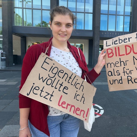 Studentin am Albertus-Magnus-Platz vor der Uni mit Plakaten, die sich gegen Sparmaßnahmen im Bildungsbereich wenden