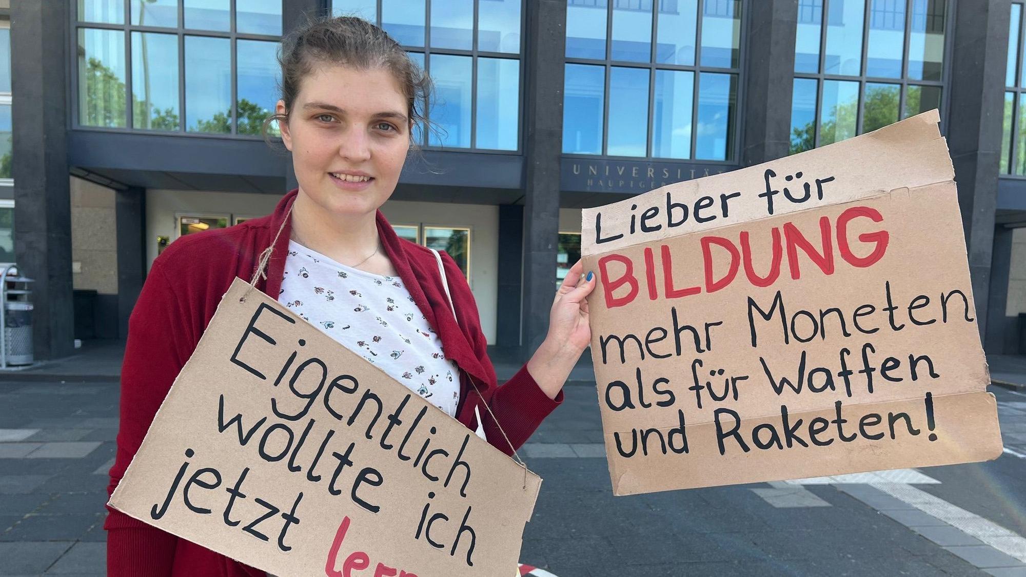 Studentin am Albertus-Magnus-Platz vor der Uni mit Plakaten, die sich gegen Sparmaßnahmen im Bildungsbereich wenden