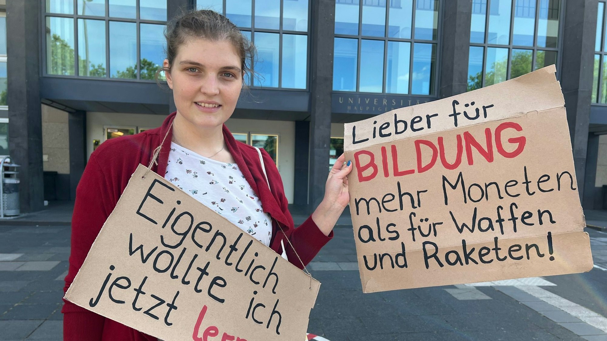 Studentin am Albertus-Magnus-Platz vor der Uni mit Plakaten, die sich gegen Sparmaßnahmen im Bildungsbereich wenden