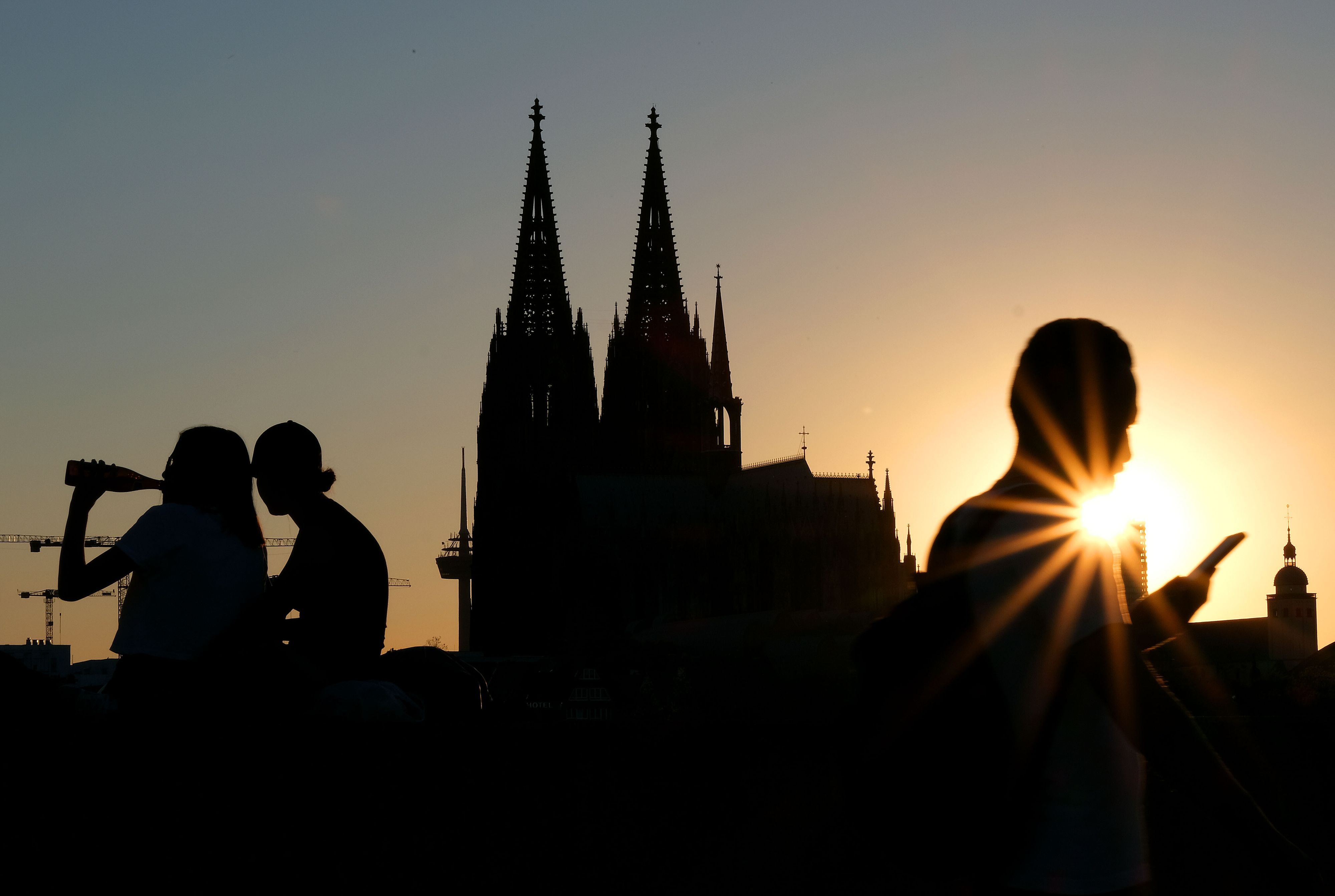 Menschen genießen im Sonnenuntergang am Rheinboulevard vor dem Dom die Abendstimmung. (Archivbild)