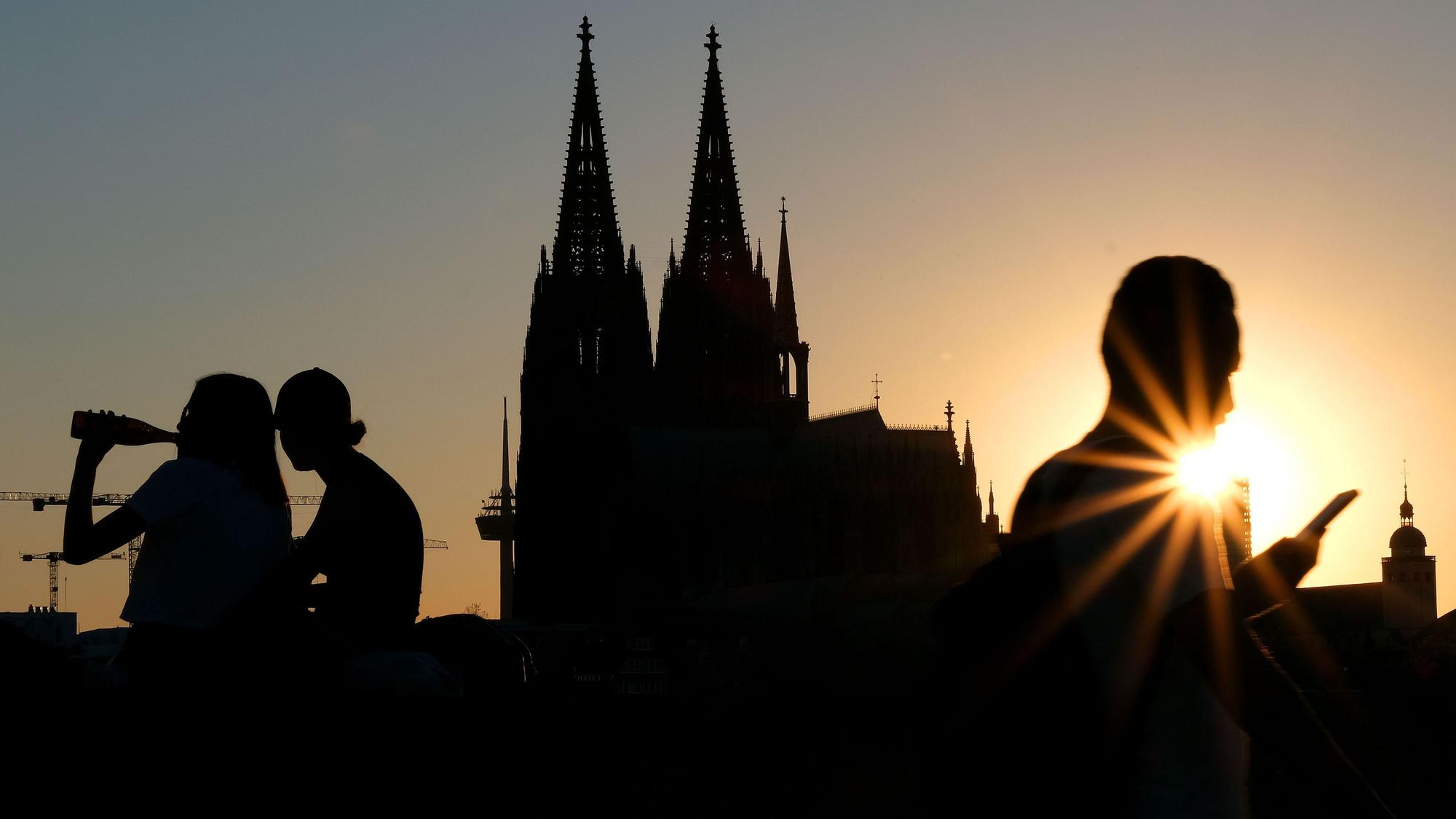 Menschen genießen im Sonnenuntergang am Rheinboulevard vor dem Dom die Abendstimmung. (Archivbild)
