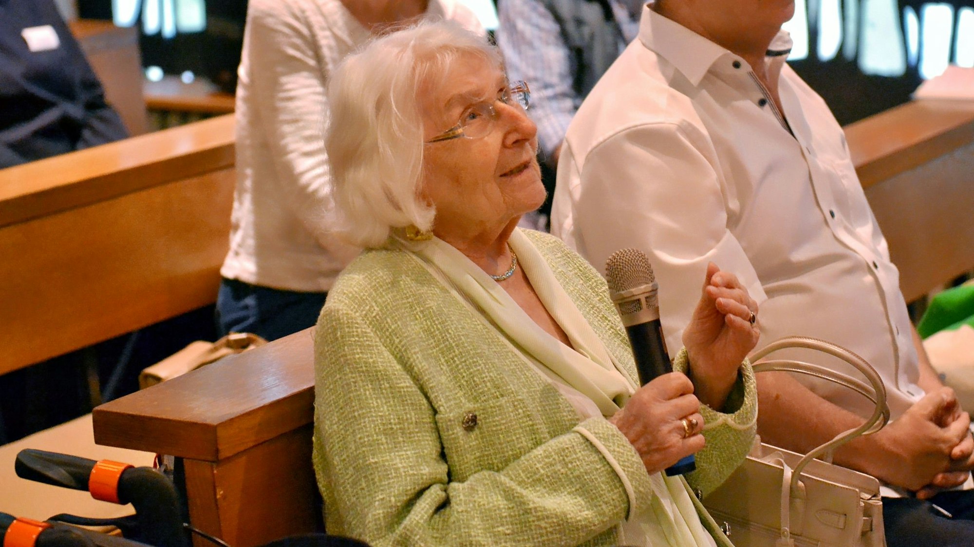 Adelheid Funke, eine ältere Dame, sitz auf einer Kirchenbank und hält ein Mikrofon.