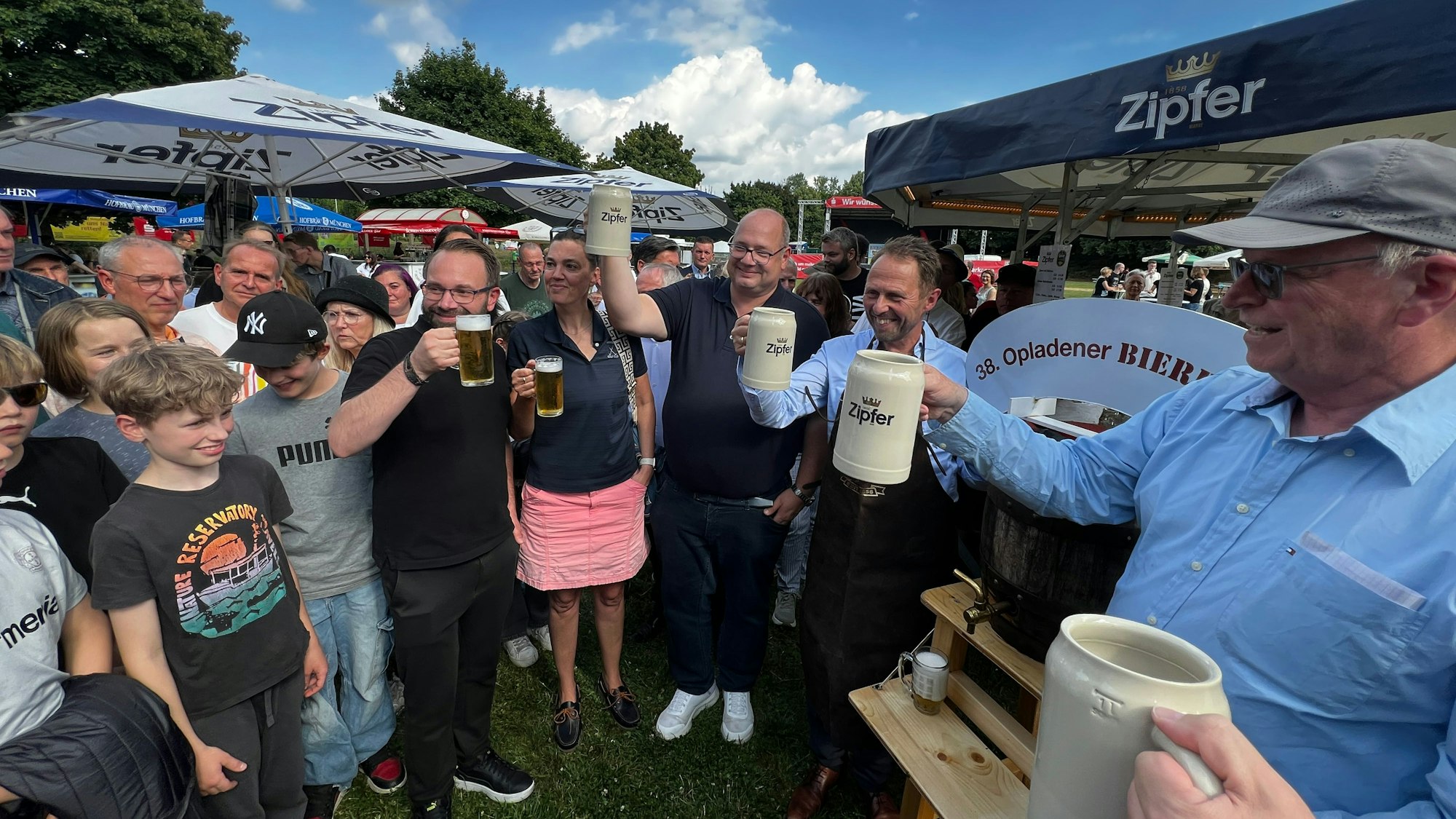 Männer und Frauen prosten sich mit Bierhumpen zu.