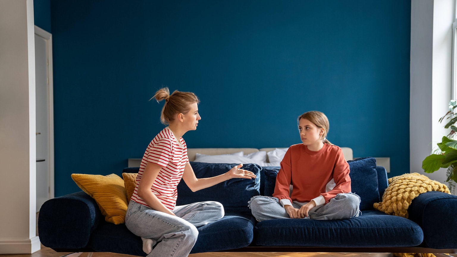 Aufgeregte Mutter, die sich mit ihrem auf dem Sofa sitzenden Kind streitet.