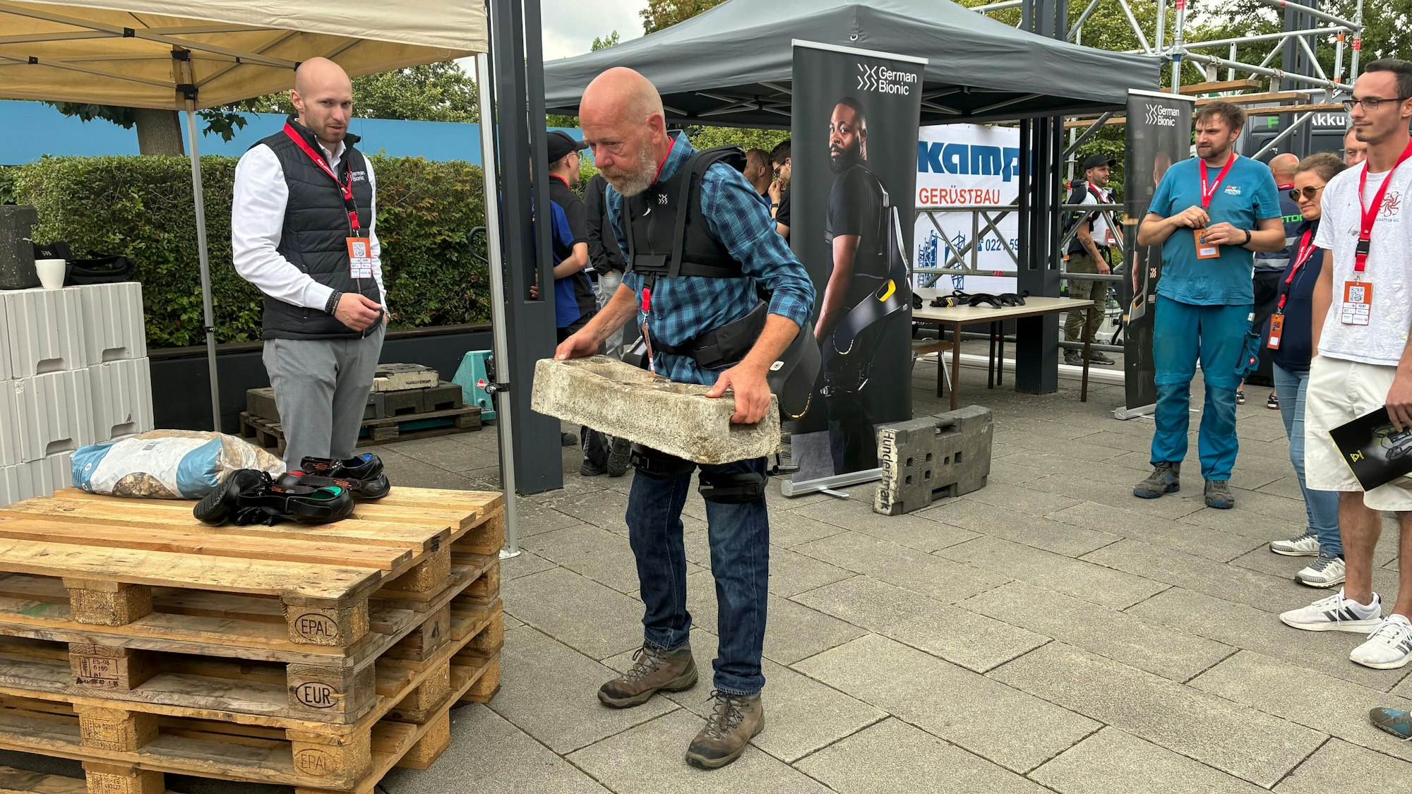 Der Tischler Manfred Kreinjobst kann seinen Beruf nicht mehr ausführen, weil er von Jahrzehnten der Arbeit Hüftprobleme hat. Bei der Handwerkskammer Köln hebt er einen 35 Kilogramm schweren Betonfuß mithilfe eines Exoskeletts mühelos hoch.