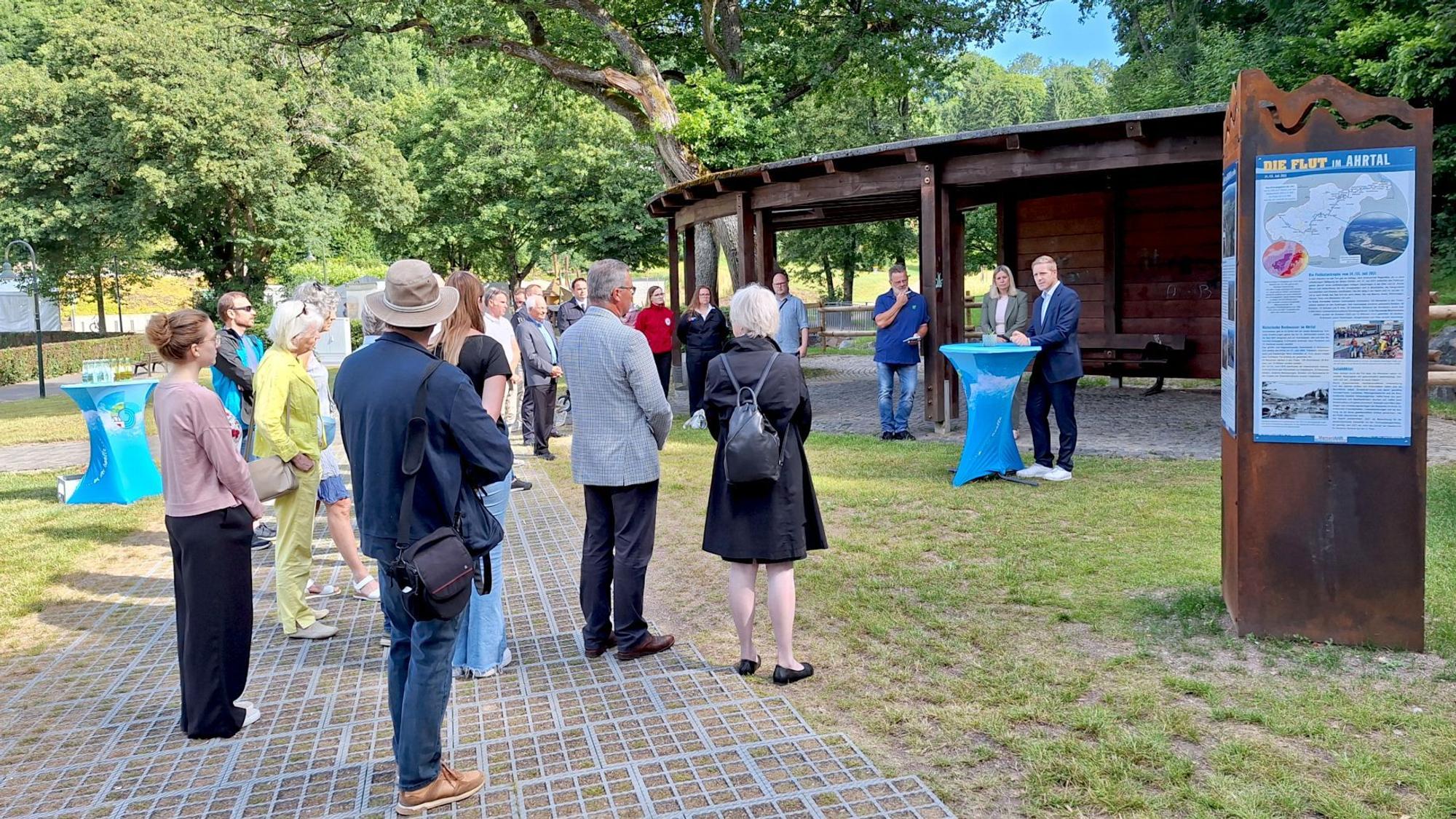 Eine Gruppe Menschen steht im Halbkreis um ein Rednerpult, an dem Landrat Markus Ramers steht. Im rechten Bildrand befindet sich eine Stele.