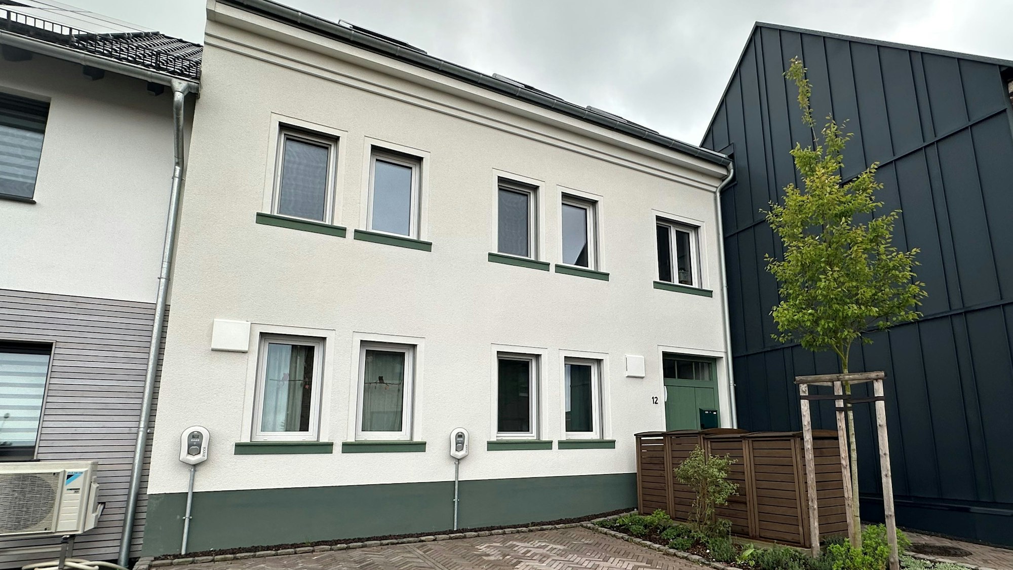 Zu sehen ist ein weißes Haus mit grünen Details an einer Straße.