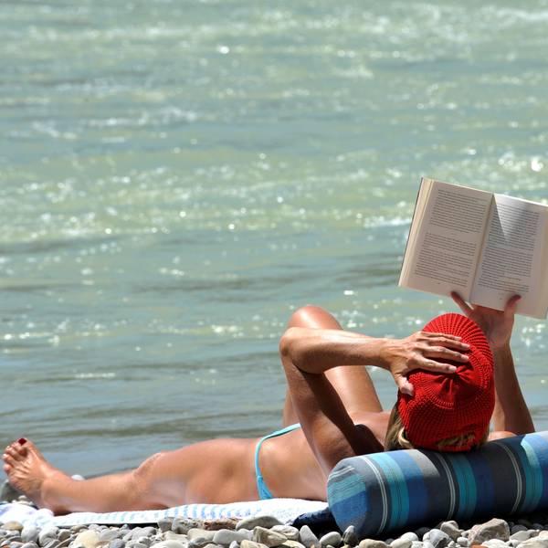 Eine Frau liest am Ufer ein Buch im Sonnenschein.