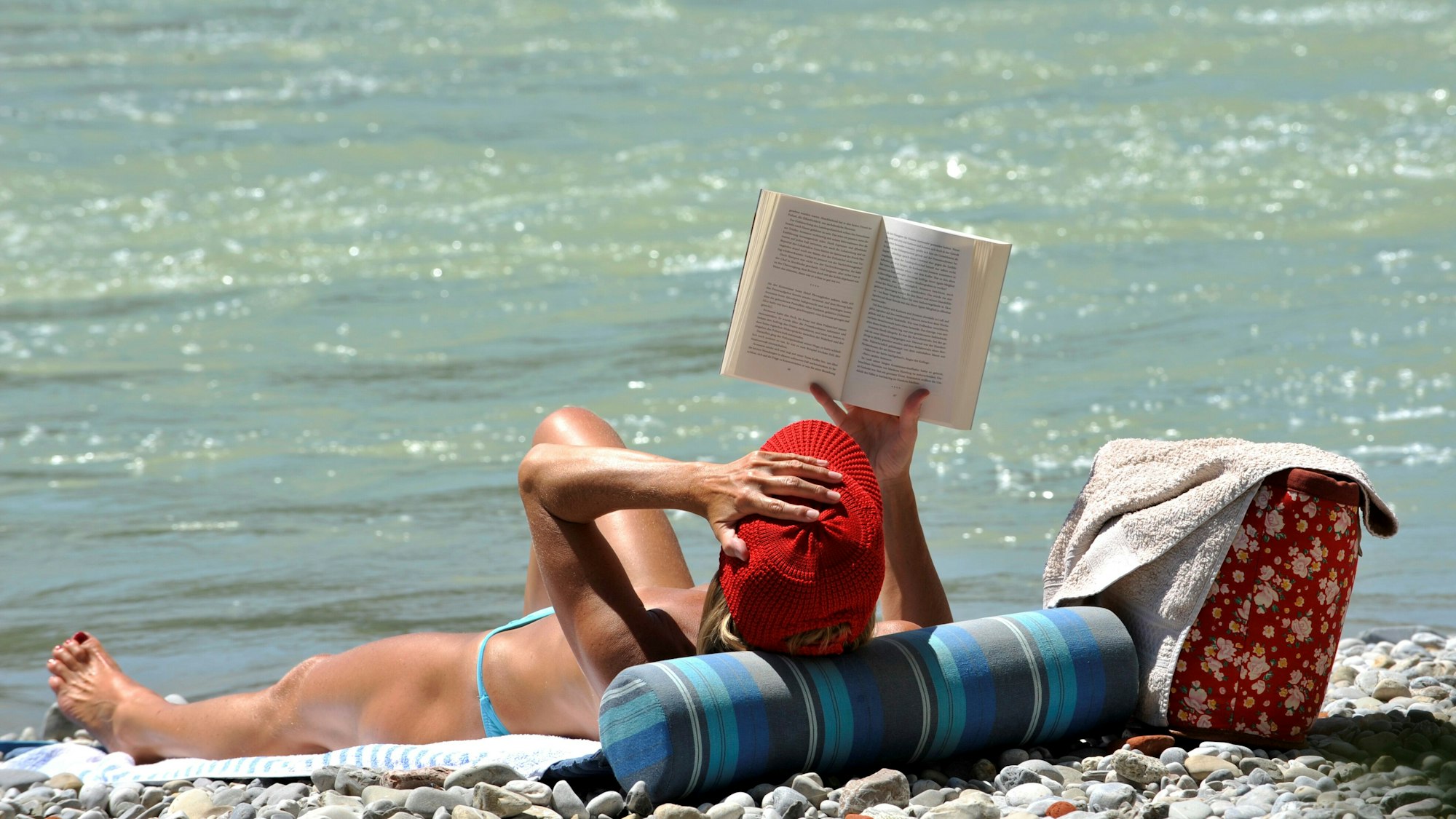 Eine Frau liest am Ufer eines Flusses in Badekleidung ein Buch.