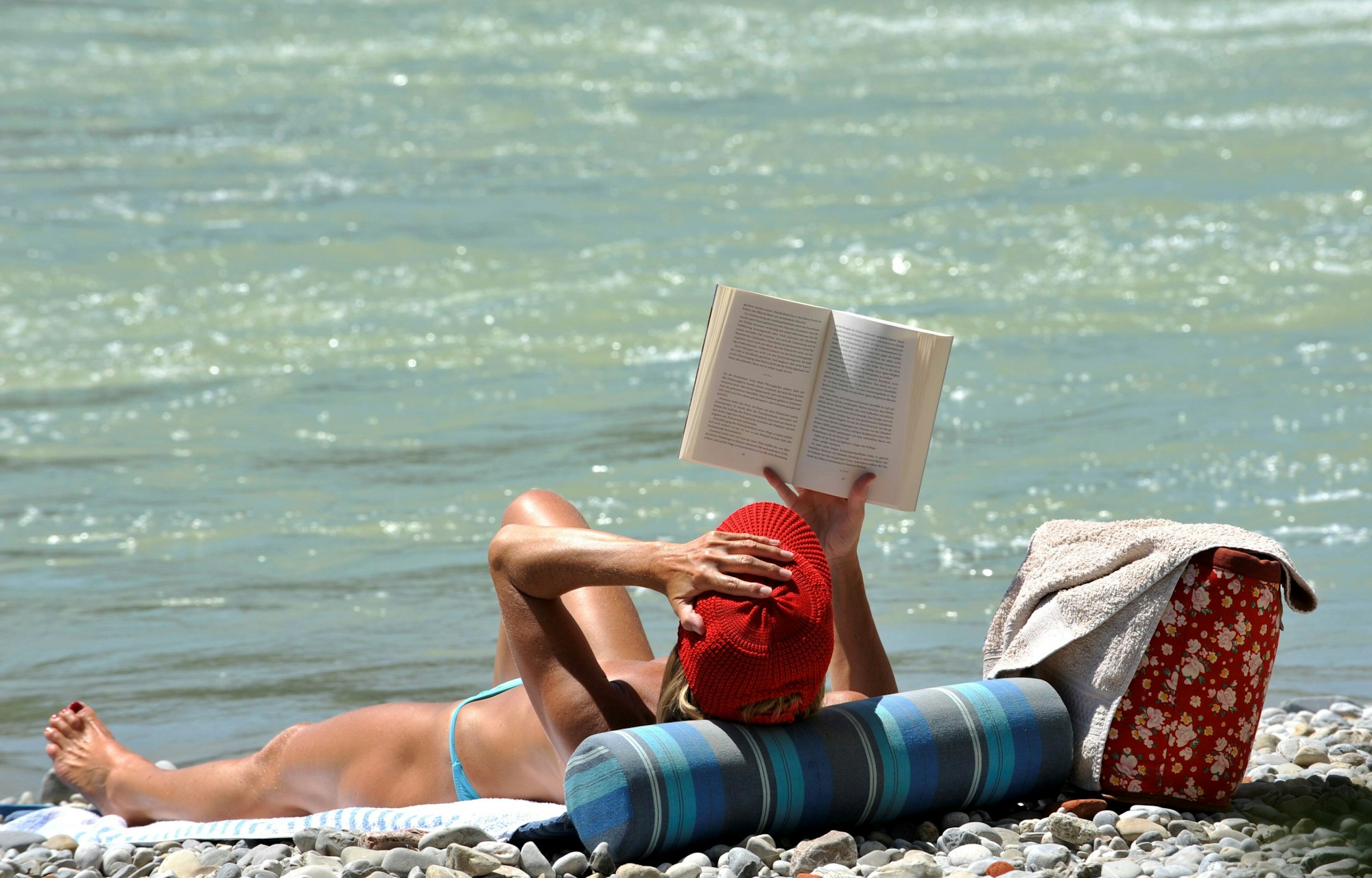 Eine Frau liest am Ufer ein Buch im Sonnenschein.