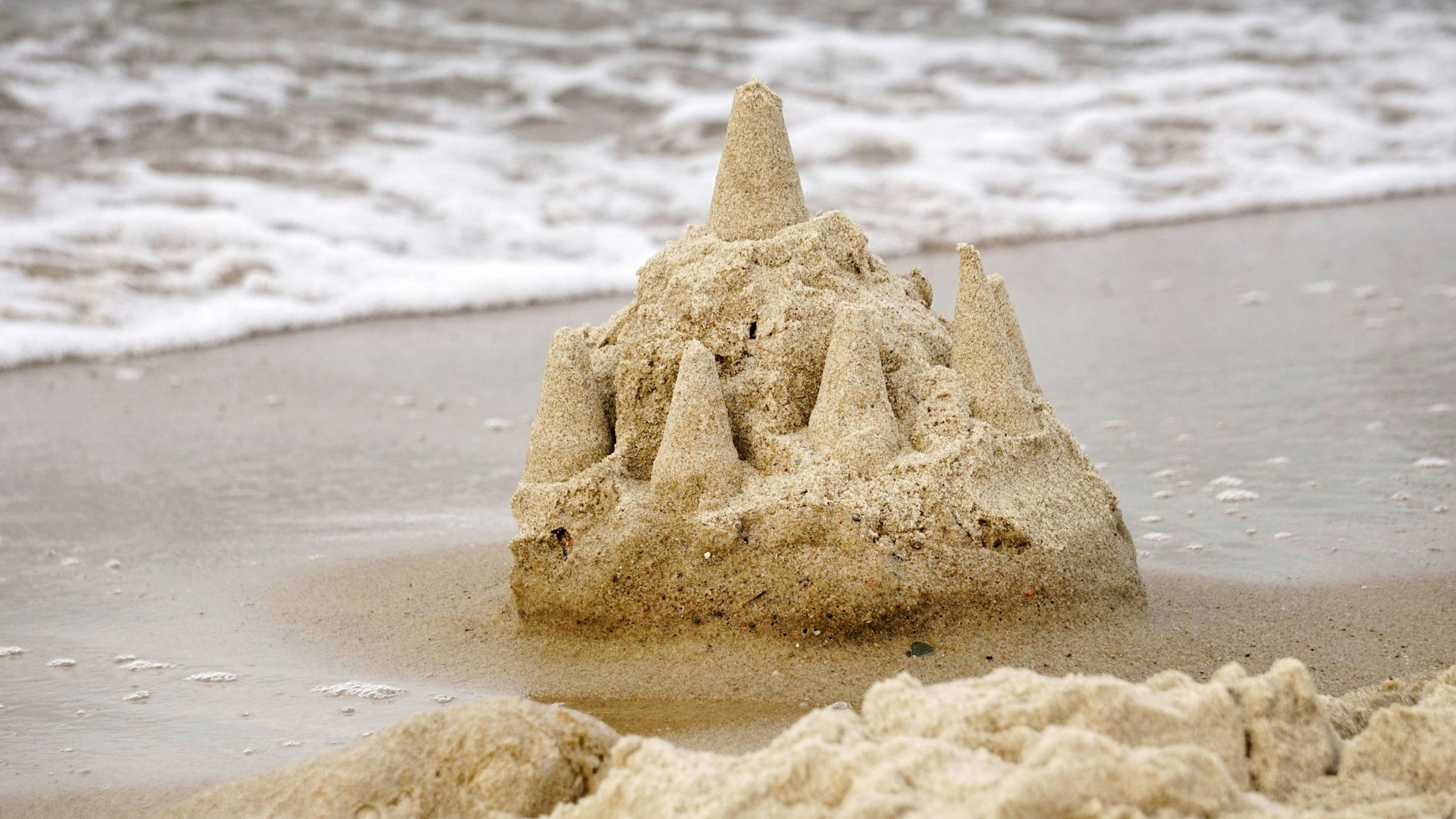 Sandburg am Wassersaum eines weißen Sandstrandes