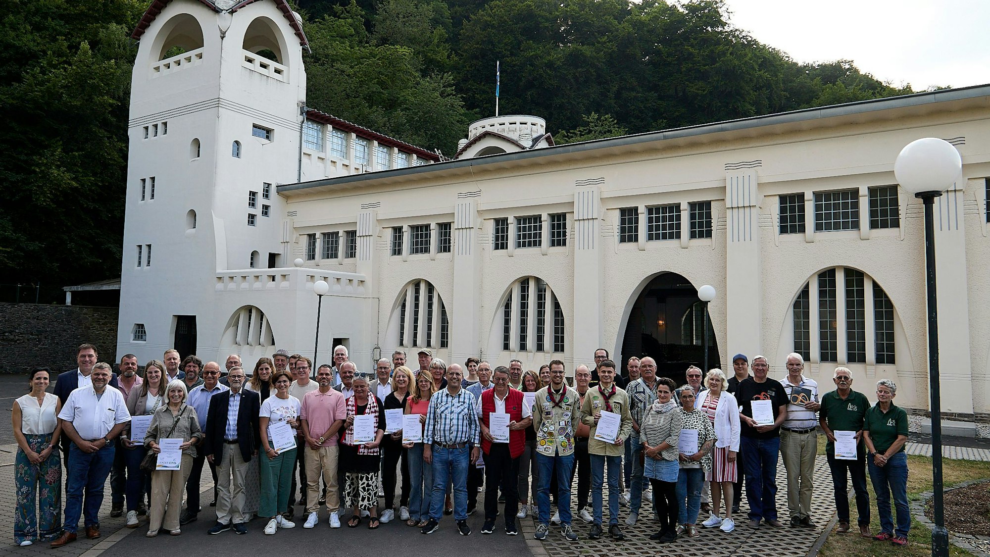 Eine Gruppe steht vor dem Jugendstilkraftwerk in Heimbach, das vor einem Wald liegt.