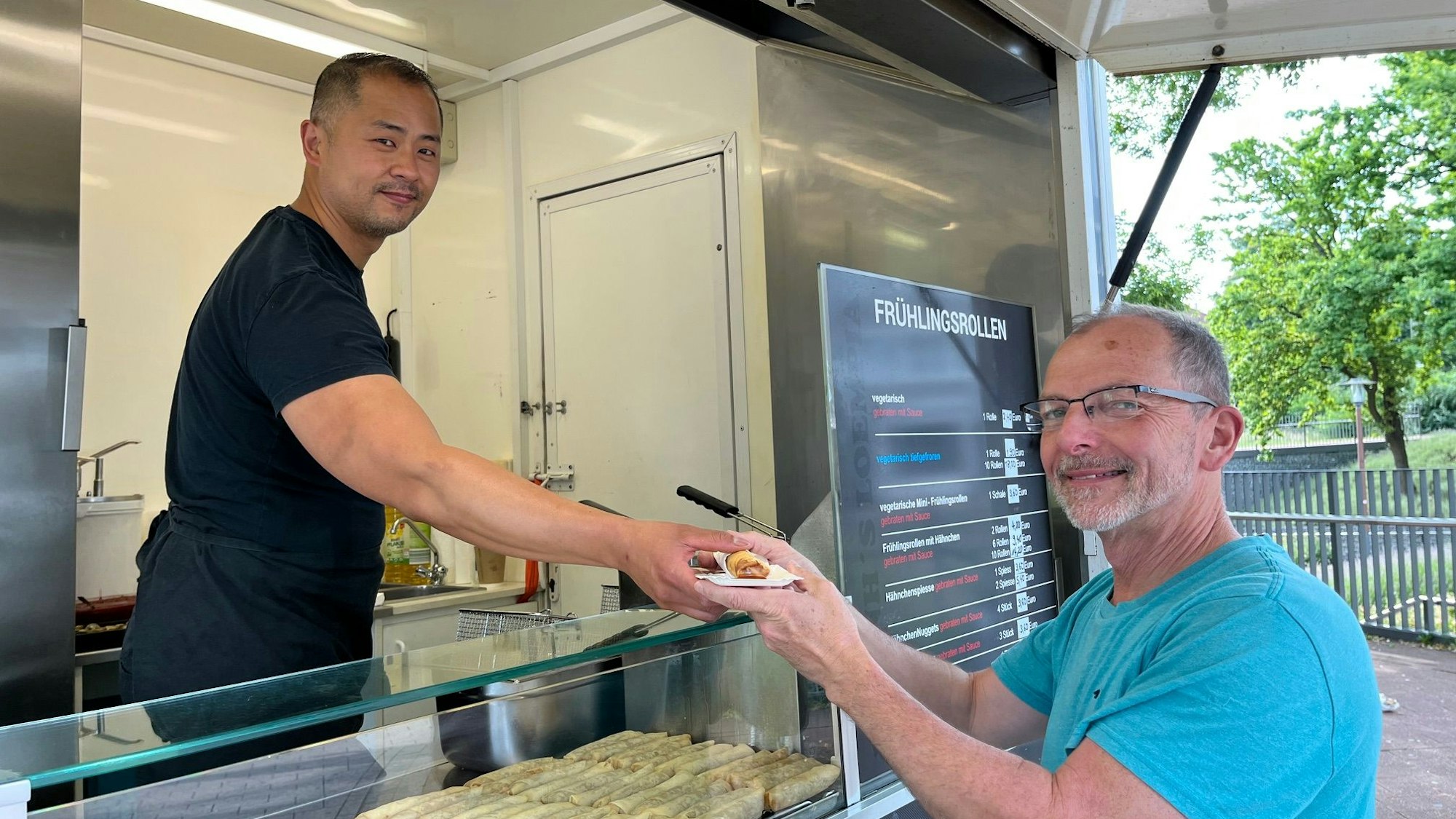 Zu sehen ist Qui Huynh, der einem Kunden eine Frühlingsrolle anreicht.