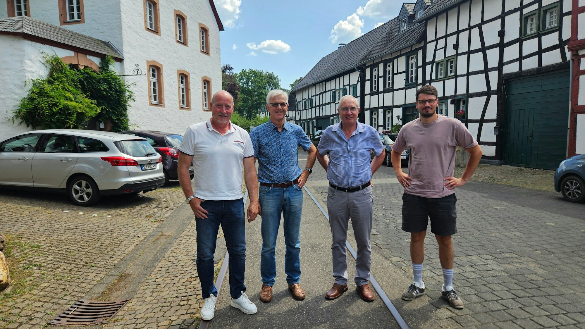 Rudi Huth, Dr. Manfred Wolter, Peter Rauw und Jan Griskewitz stehen nebeneinander auf Bahngleisen, die inmitten von Fachwerkhäusern und einem anderen Gebäude verlaufen.