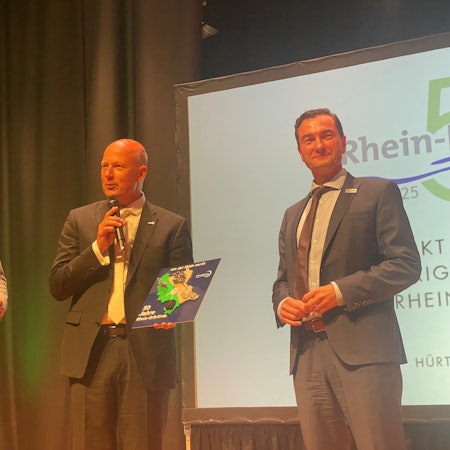 Zu sehen sind Moderator Olly Hahn sowie Frank Rock und Dr. Thomas Wilk auf der Bühne.