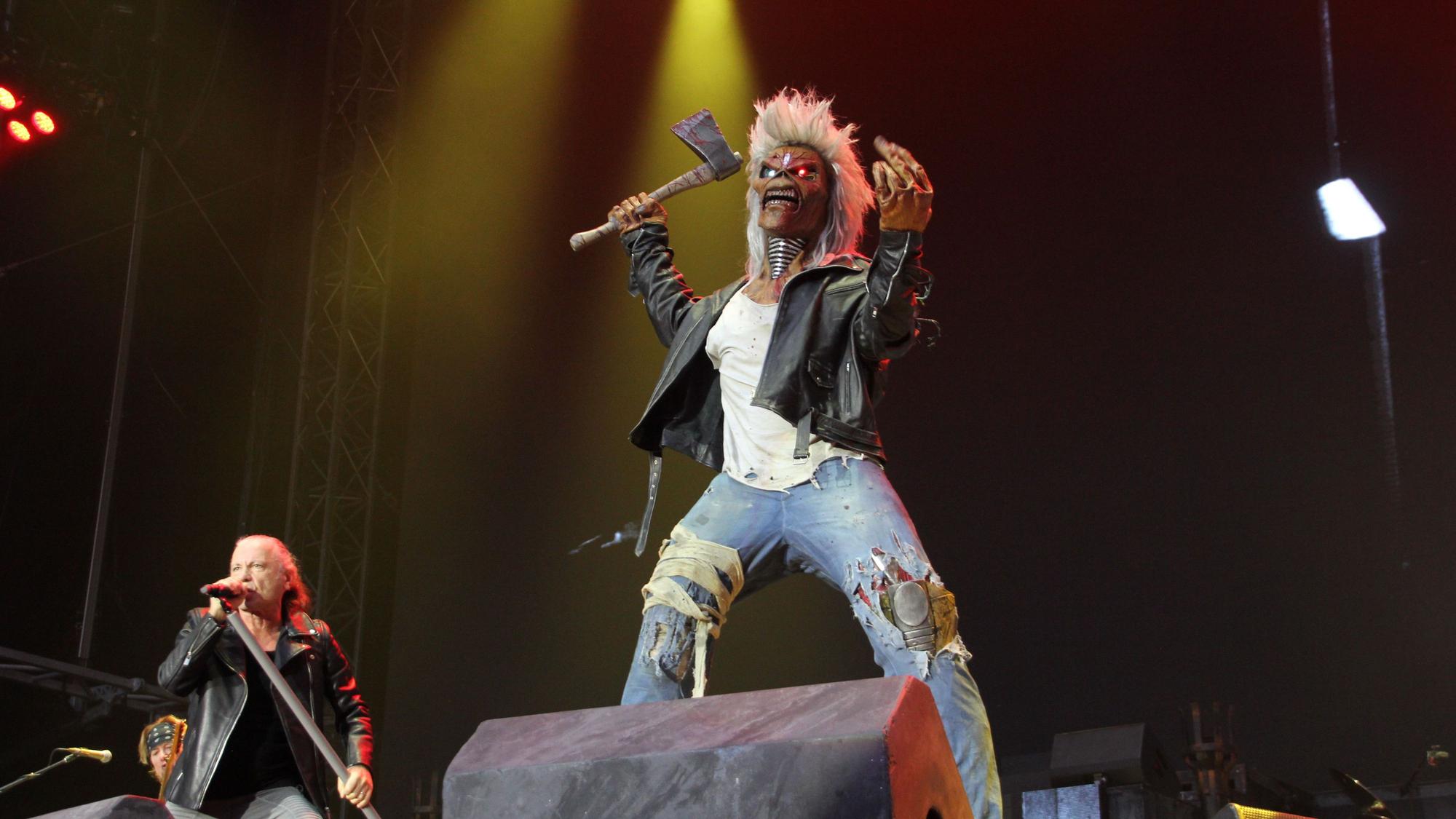 Das Maskottchen der Band Iron Maiden ist ein überlebensgroßes Monster. Er steht auf der Bühne und schwingt bedrohlich eine blutgetränkte Axt. Rechts von Eddie steht Sänger Bruce Dickinson am Mikrofon.