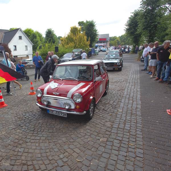 Eine Frau mit Flagge gibt das Startsignal für einen alten Minicooper.