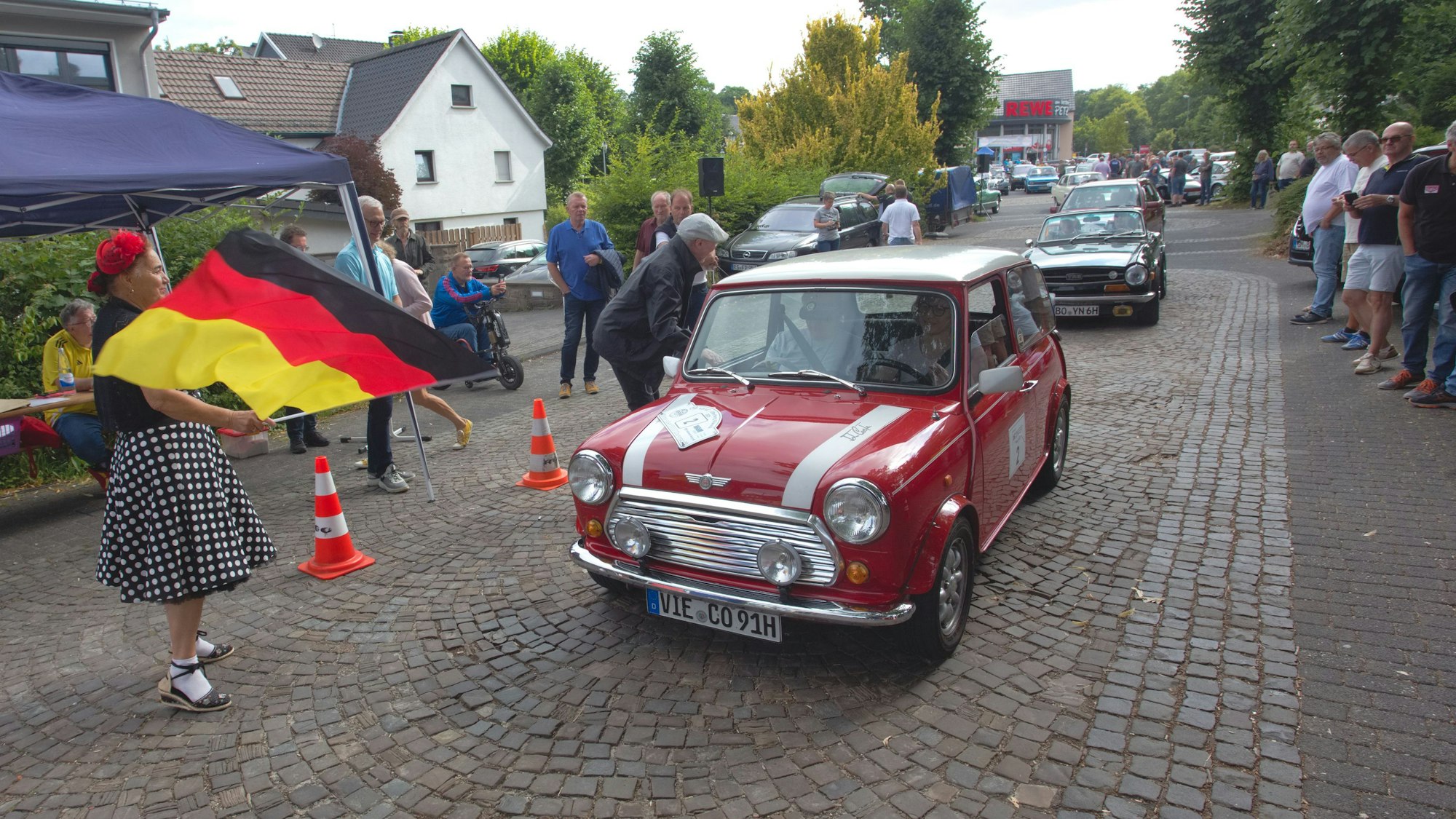 Eine Frau mit Flagge gibt das Startsignal für einen alten Minicooper.