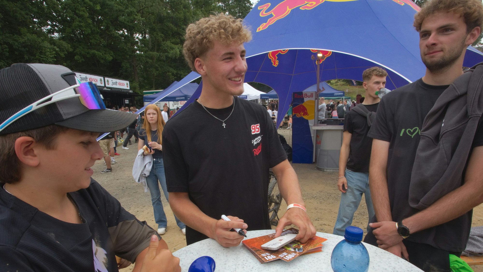 Ein Motocrossfahrer steht an einem Stehtisch und schreibt Autogramme.