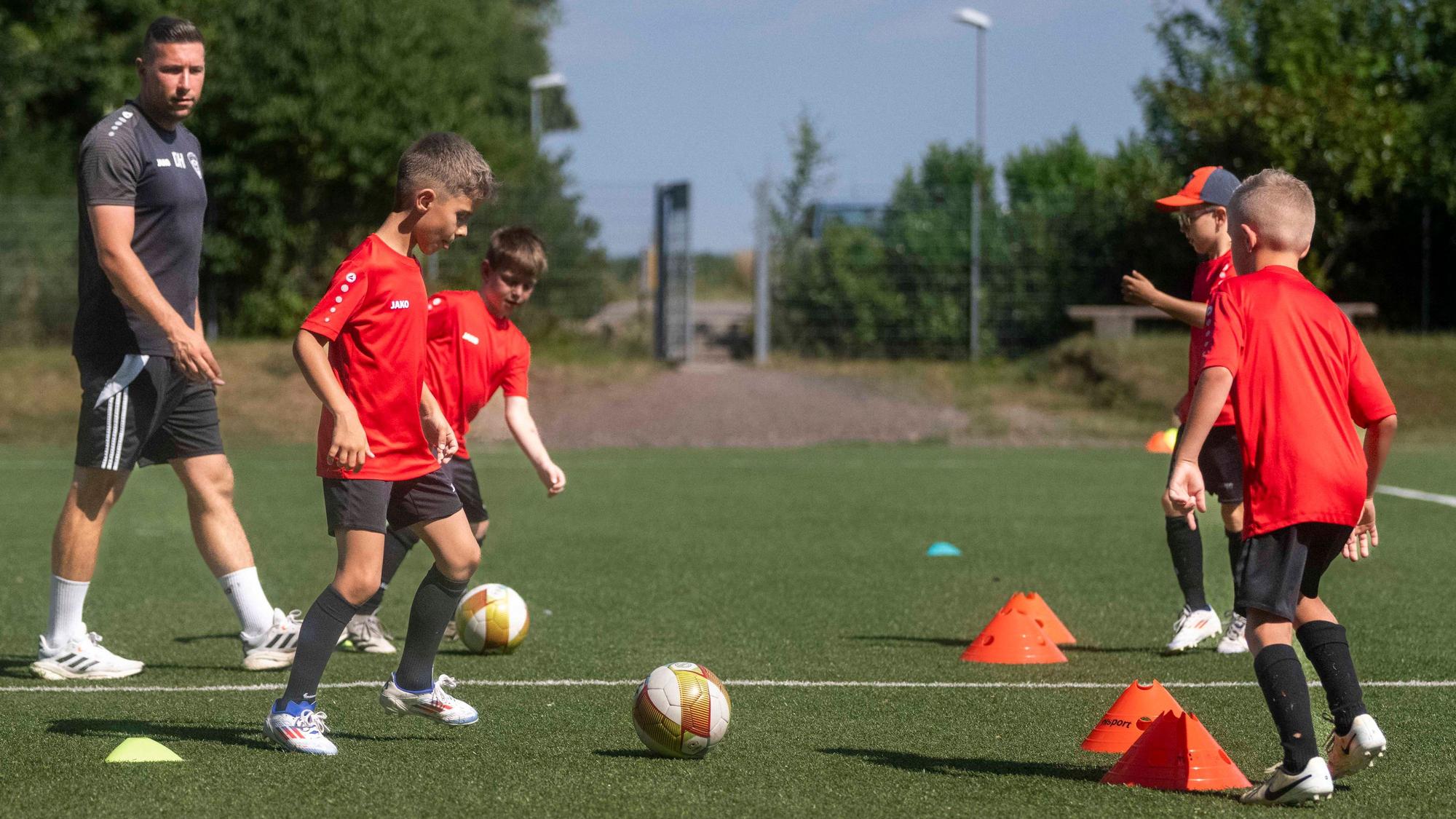 Junge Fußballspieler passen sich Bälle durch Hütchen hindurch zu. Der Trainer beobachtet die Fußballer.