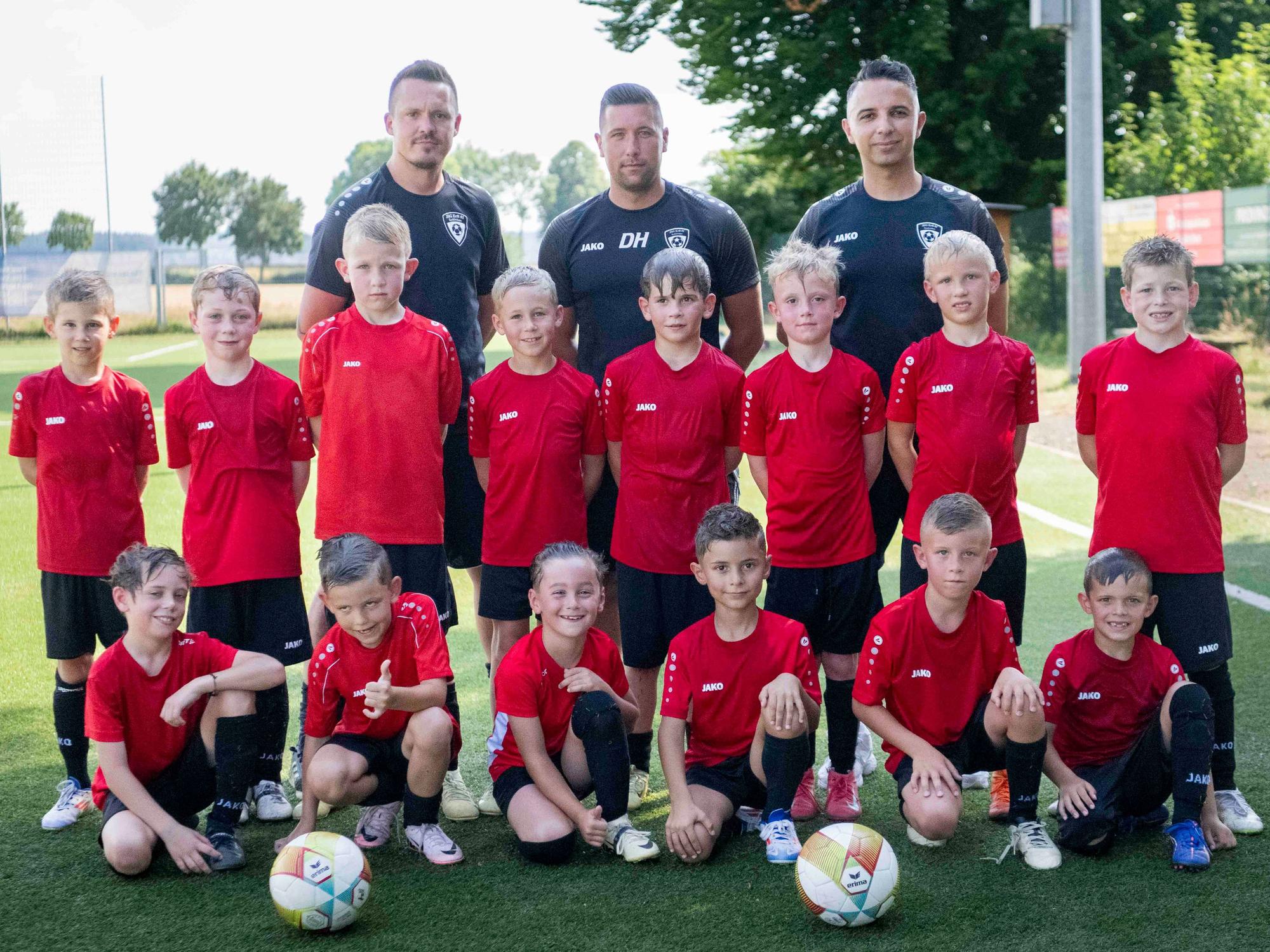 Die Mannschaft der U8 der JSG Erft 01 Euskirchen hat sich zum Gruppenfoto aufgestellt. Im Hintergrund steht das Trainerteam, ganz vorne kniene sechs Spieler, dahinter stehen acht.