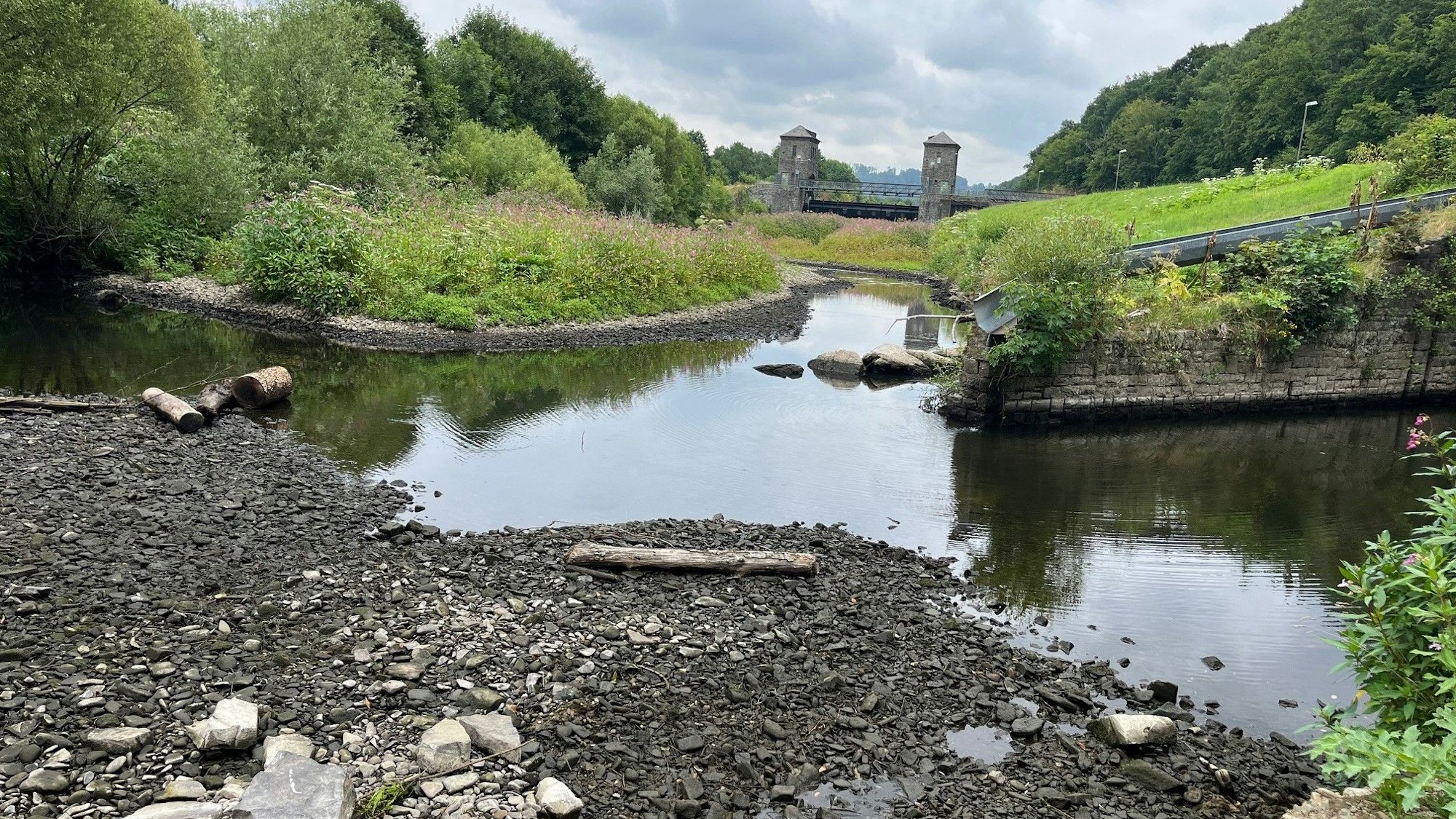 Man sieht ein Gewässer, das sich zurückgezogen hat, im Hintergrund ein Staugebäude.