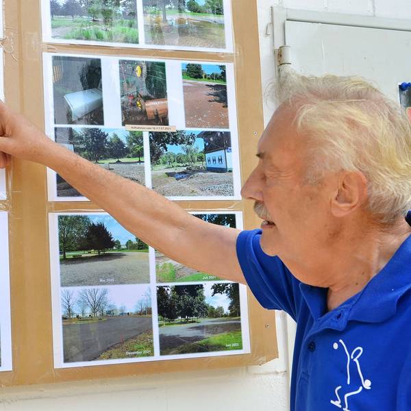 Wolfgang Vieweg zeigt auf Aufnahmen der Flutkatastrophe 2021, die an einer Wand hängen.