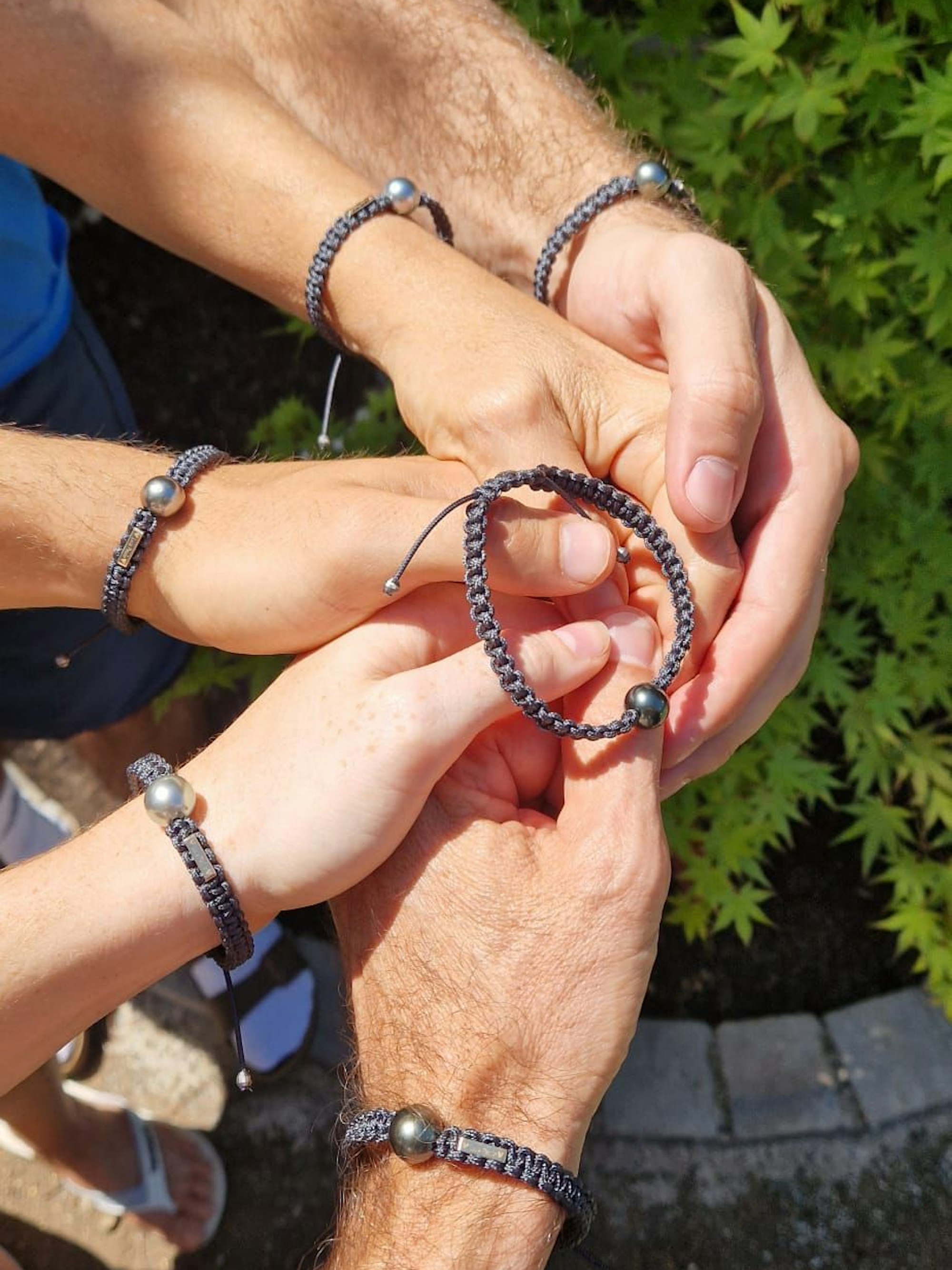 Auf dem Bild sind Hände zu sehen, die alle ein Armband tragen.