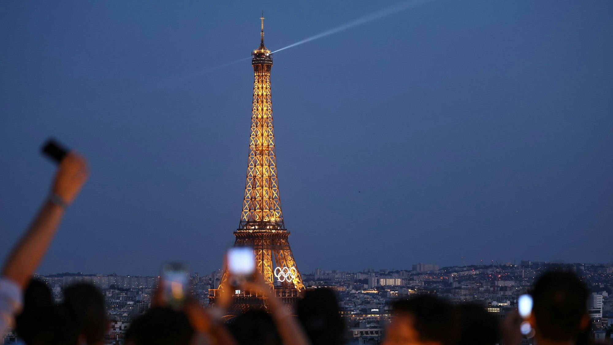 Zahlreiche Touristen fotografieren den Eiffelturm mit den Olympischen Ringen von der Terrasse des Arc de Triomphe de l’Étoile.