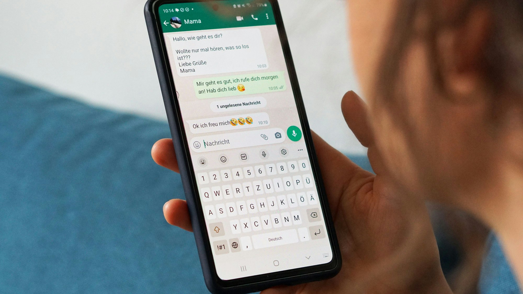 Eine junge Frau hält ihr Smartphone in der Hand und liest eine Whatsapp-Nachricht von ihrer Mama.