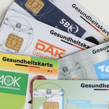 Gesundheitskarten verschiedener Krankenkassen liegen auf einem Tisch.