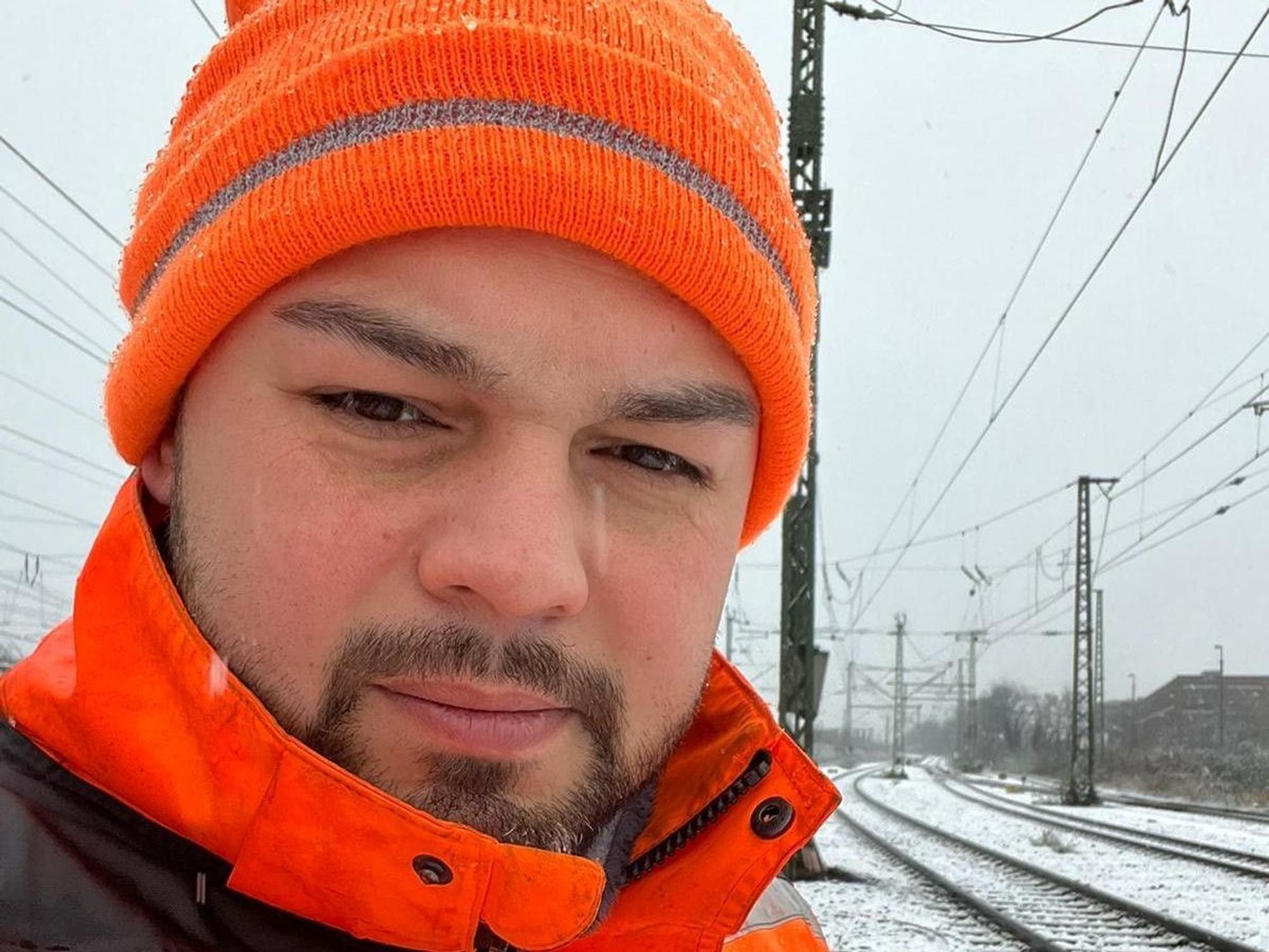 Ein Mann steht im Winter an Bahngleisen.