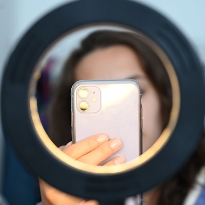 Eine Influencerin sitzt hinter einem Ringlicht und macht dabei Aufnahmen von sich.