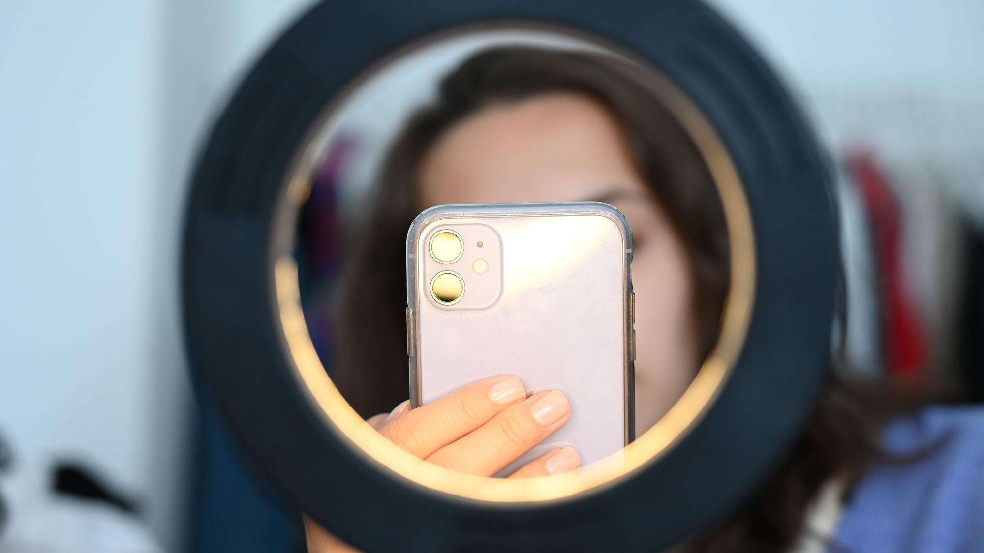 Eine Influencerin sitzt hinter einem Ringlicht und macht dabei Aufnahmen von sich.