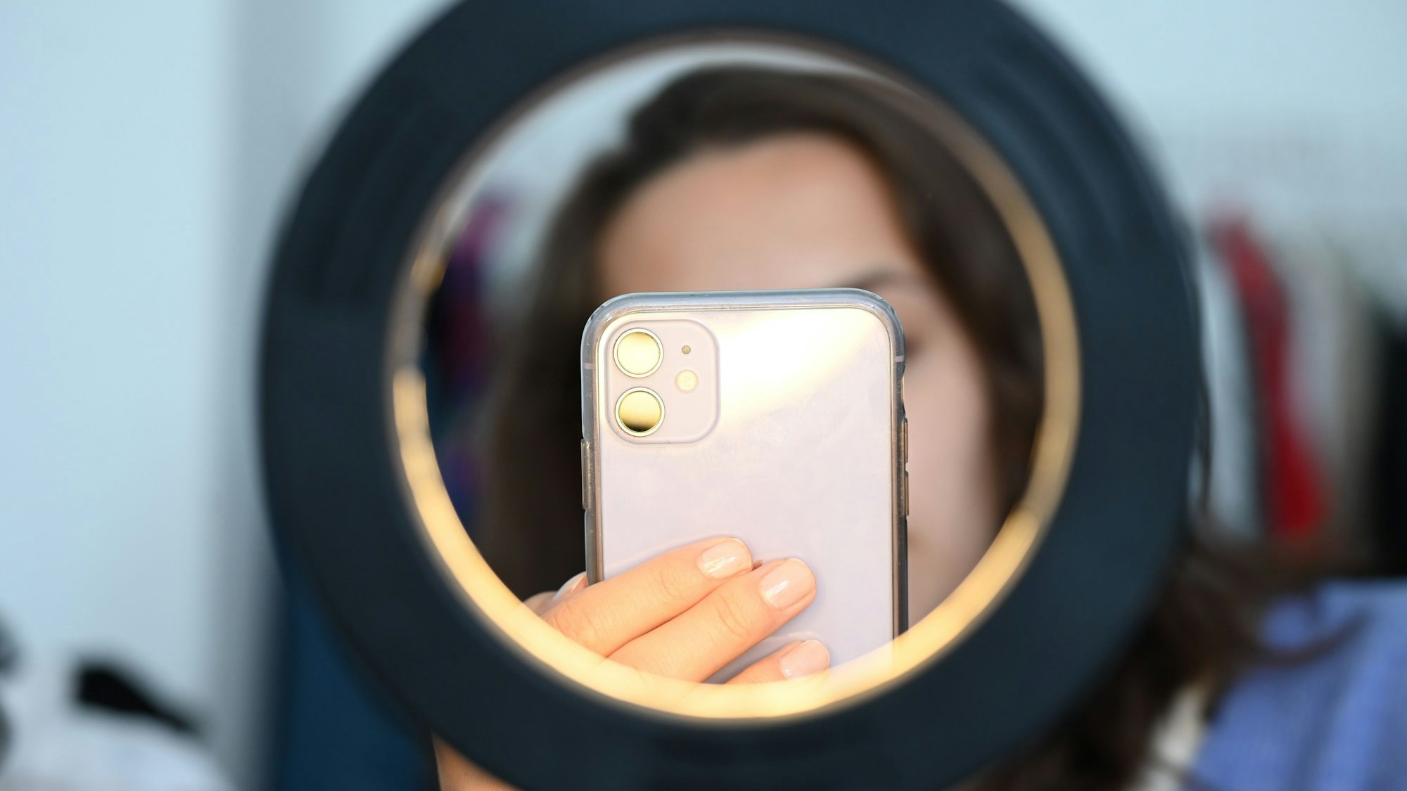 Eine Influencerin sitzt hinter einem Ringlicht und macht dabei Aufnahmen von sich.