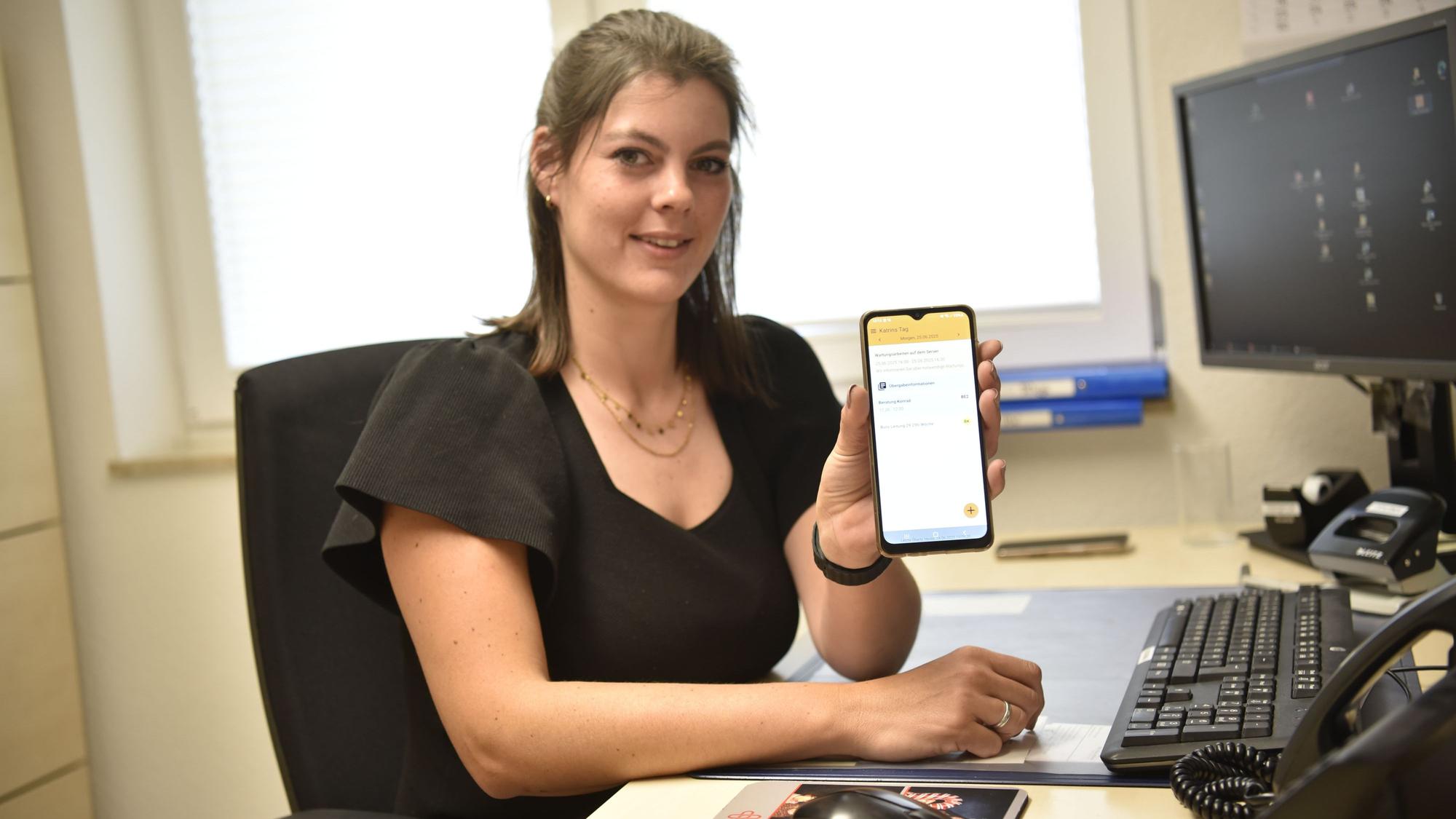 Katrin Konrad, Teamleiterin mobile Pflege bei der Marienborn in Zülpich, sitzt an einem Schreibtisch und zeigt das Display eines Smartphones.