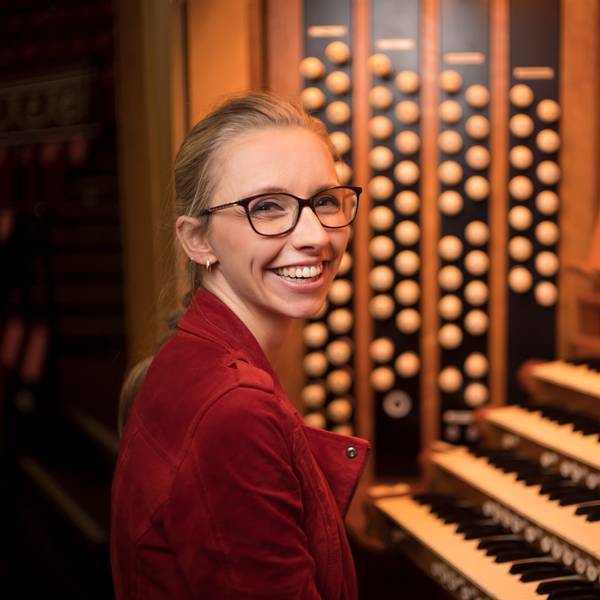 Eine Frau sitzt an einer Orgel und lächelt in die Kamera.