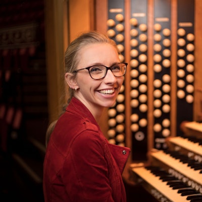 Eine Frau sitzt an einer Orgel und lächelt in die Kamera.