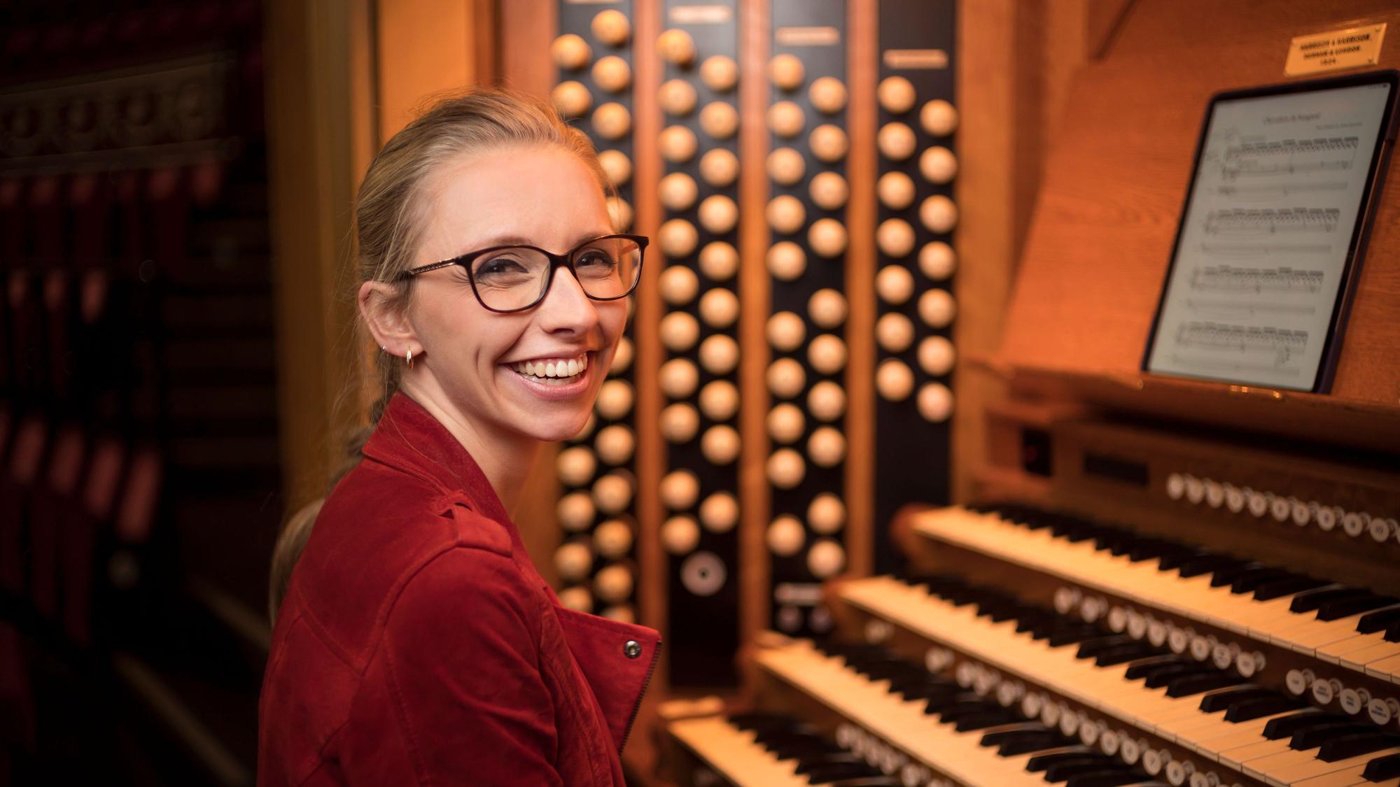 Eine Frau sitzt an einer Orgel und lächelt in die Kamera.