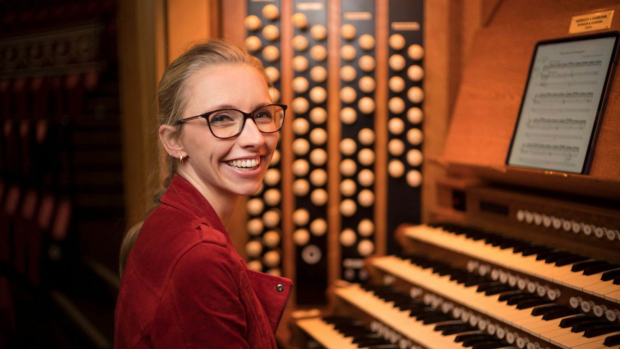 Eine Frau sitzt an einer Orgel und lächelt in die Kamera.