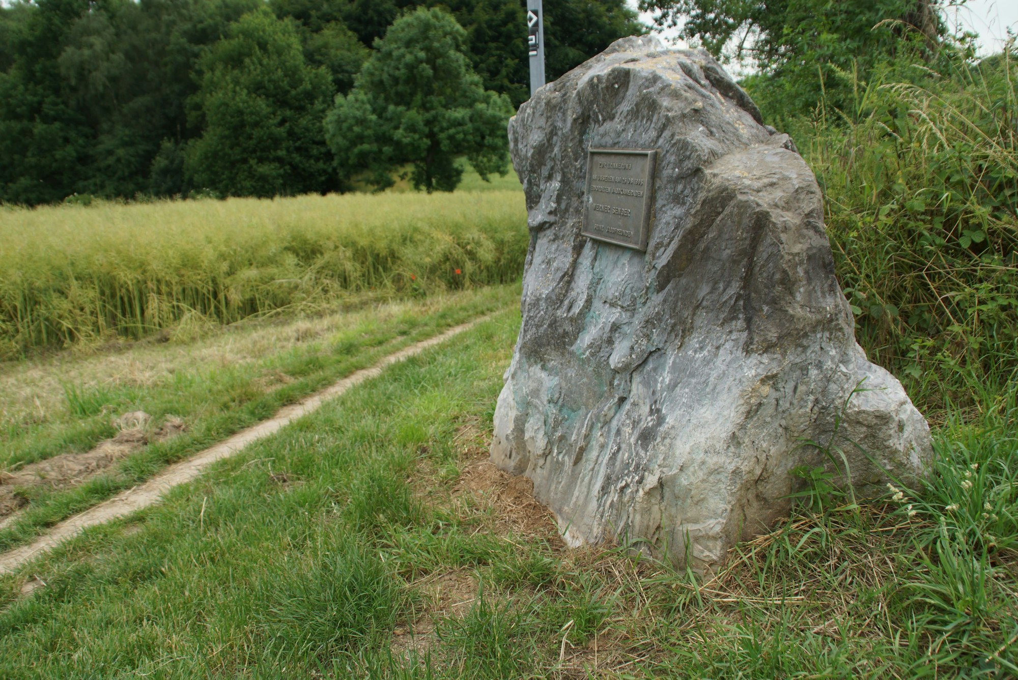 Ein Stein mit Gedenktafel an einem Feld