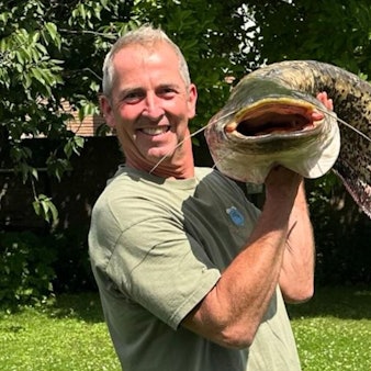 Das Bild zeigt einen Mann mit einem großen Wels in den Armen.