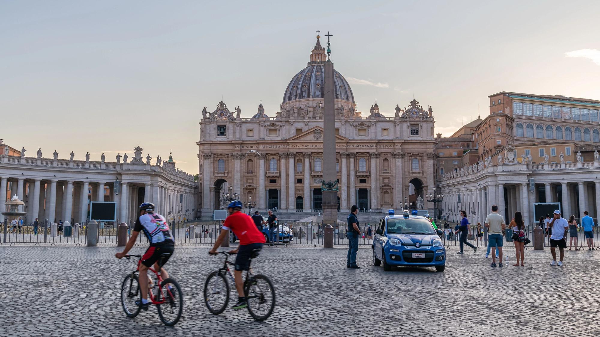 Panoramic early morning scene at St Peter's square with police car and cicylists in foreground in Rome , Italy