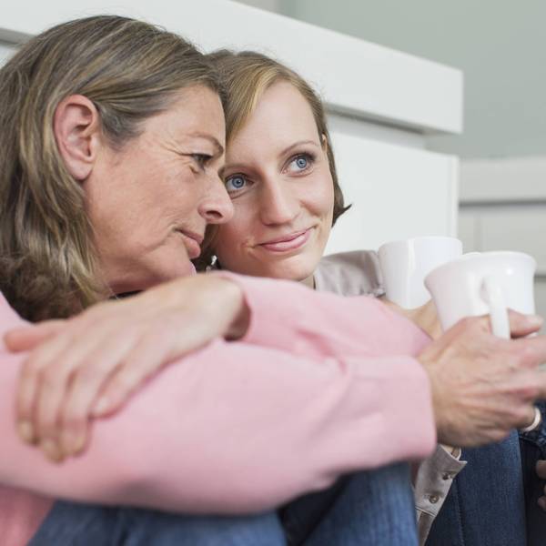 Eine ältere Frau und eine Teenagerin sitzen vor einer Wand und haben jeweils eine Tasse in der Hand.