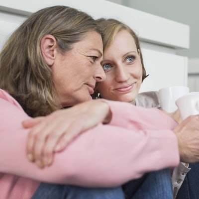 Eine ältere Frau und eine Teenagerin sitzen vor einer Wand und haben jeweils eine Tasse in der Hand.